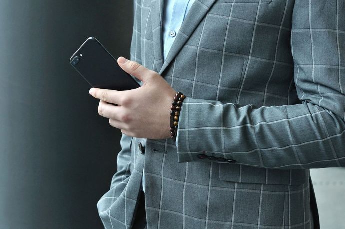 Muž v šedém saku s mobilem v ruce na které má originální BeWooden náramky